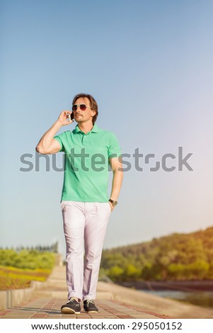 Rich man walking with mobile phone. Handsome stylish man in sunglasses talking on smart phone looking away.