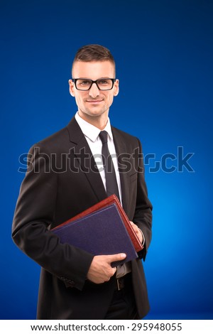 Smiling businessman standing with documents in his hands. Busy man in glasses and business suit on blue background.