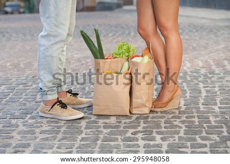 Young couple waiting for bus after shopping. Man and woman standing near the bags full of products for picnic.