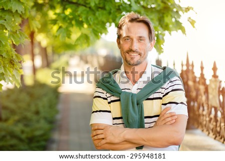 Young and handsome rich man resting in the green park. Man with his arms crossed smiling because of wealthy lifestyle.