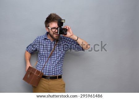 Handsome young man traveller making photos. Smiling man in navy blue shirt posing with brown cross-body bag on grey.