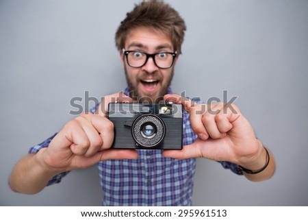 Close-up photo of young man traveller\'s camera. Man in navy blue plaid shirt making photos and big smiling isolated on grey.