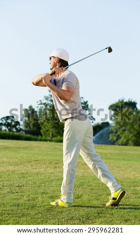 Man playing golf on beautiful sunny green golf course. Hitting golf ball down the fairway from the tee with driver.