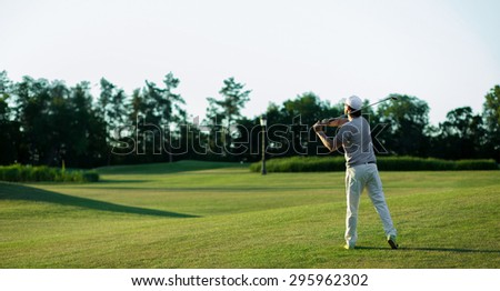 Golf player teeing off. Man hitting golf ball from tee box with driver isolated on sunny green golf course.