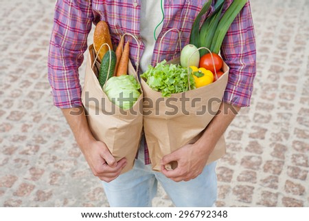 Close-up profile of bags full of fruits and vegetables. Young man carrying bags in his hands after shopping.