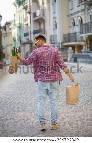 Profile of young man\'s back in sunglasses. Handsome man lifting bag full of food with his left hand.