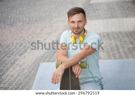Young man with his skate-board in the city centre. Short-haired man in blue T-shirt enjoying day time and beautiful weather.