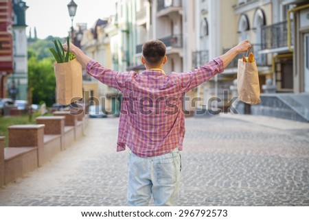 Portrait of happy man\'s back. Young man inplaid shirt carrying bags full of foods and drinks for picnic.