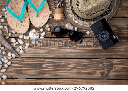 Picture of summer objects for vacation. Flip-flops, straw hat, sunglasses, photocamera are organized from low left to top right on wooden background.