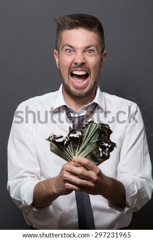 Businessman screaming with burning dollars on dark grey. Short-haired man in white shirt annoyed by bankrupcy of his company.