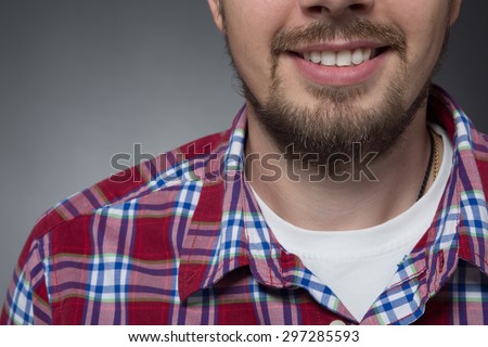 Close-up portrait of bearded man with white teeth. Model posing in maroon shirt and white T-shirt on grey background.
