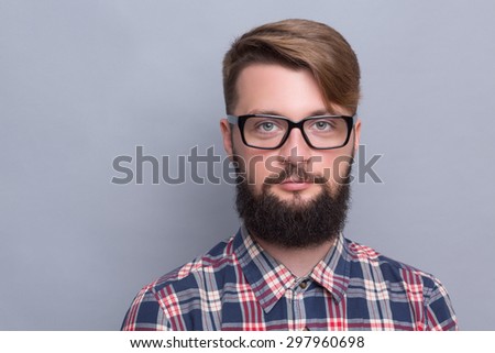 Close-up portrait of hipster bearded man. Happy man with up-to-date hairstyle posing in glasses near grey background.