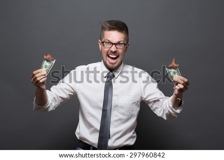 Angry businessman with burning dollars. Serious man in glasses loosing money just in his hands, man in showing his teeth and screaming.