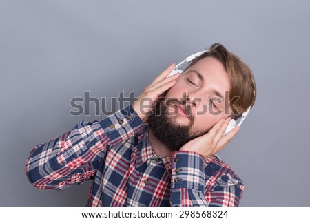 Hipster bearded man enjoying different tracks in earphones. Listening to the music making this man happy isolated on grey.