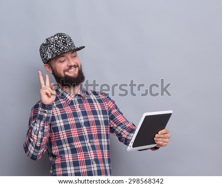 Hipster bearded man communicating with friends. Man in trucker hat showing yo sign, smiling and communicating through Skype.
