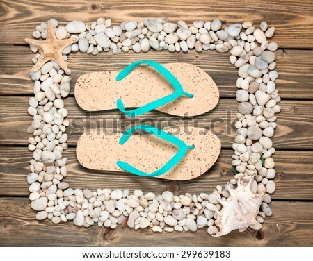 Picture of summer flip-flops in the centre of frame from seashells and stones. Frame made of shells isolated on wooden background.