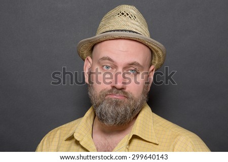Profile of sad bearded man in straw hat. Bold gloomy man in yellow shirt is dissatisfied on dark grey background.