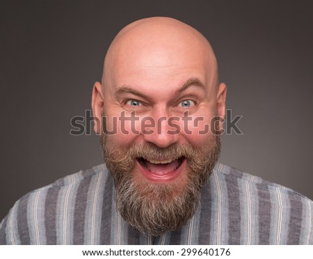 Bold jailbird big laughing. Bearded man with red face opened his face and smiling with annoyance on dark grey.