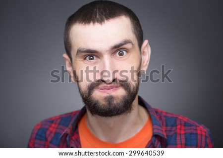 Hipster bearded man puffing cheeks on dark grey. Short-haired man with earring enjoying his daytime, he looks so funny.