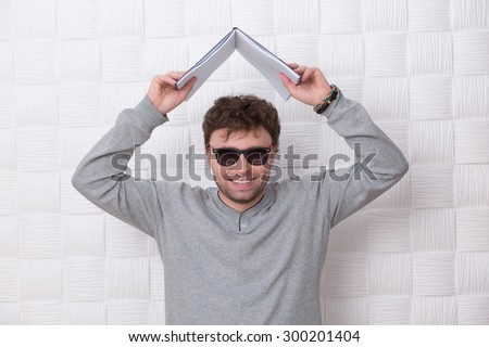Handsome man posing with register above his head. Cute man in sunglasses happy laughing, because he is successful in his life.