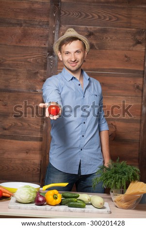 Chef holding tomato in his hand on wooden. Smiling man with straw hat on preparing food with fresh vegetables.