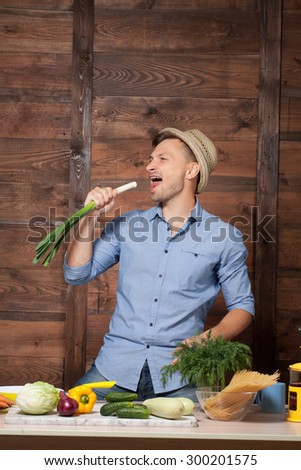 Chef having fun preparing healthy food with fresh vegetables. Man with straw hat on smiling with leek isolated over wooden background. Gourmet.