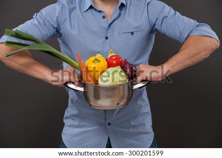 Close-up picture of pan with fresh vegetables. Man in blue shirt demonstrating products for meals he is goint to prepare and cook.