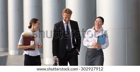 Businesspeople communicating while walking on the territory of office building. Two woman in white shirts and man in black suit smiling.