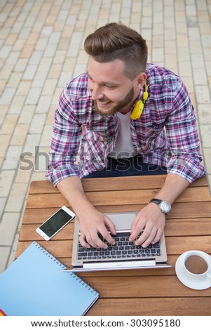 Photo of handsome hipster man browsing the Internet on laptop. Bearded man sitting in the cafe with a cup of americano coffee with milk.
