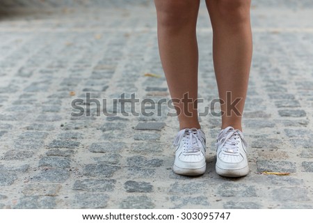Close-up picture of young woman\'s legs in the street. Woman in white training shoes walking.
