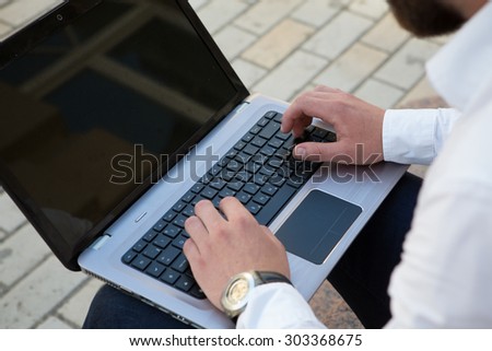 Close up male hands using laptop computer outdoors. Freelancer man browsing the Internet with the help of city wi-fi.