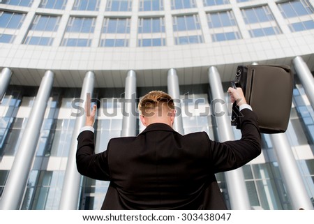 Portrait of king of the world with his hands raised. Young successful businessman in front of the office building with brief case.