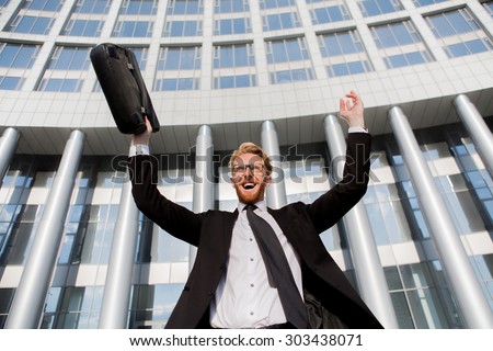 Successful businessman with arms up celebrating the victory. Smiling man in black business suit and brief case screaming from hapiness.