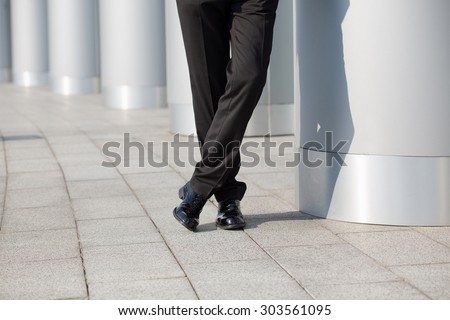 Low section image of successful business person\'s legs. Man in black business suit posing with his legs crossed near column.