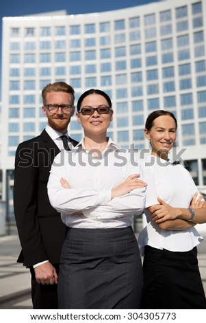 Office, business and teamwork concept. Friendly young smiling businesswoman in sunglasses with team on back with her arms folded.