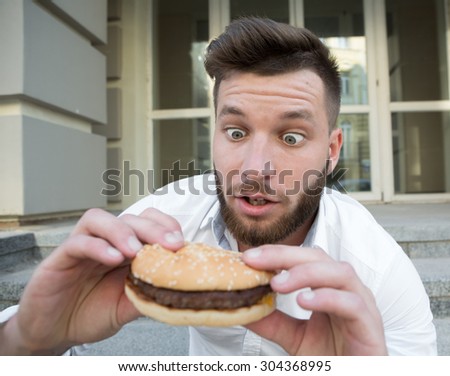Handsome young man dreaming of tasting delicious cheeseburger very much. Surprised man looking at it with excitement.