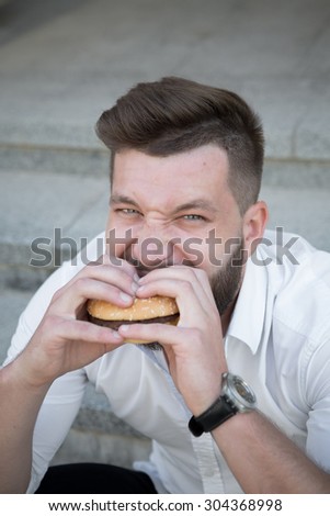 City hipster businessman eating hamburger. Close-up portrait of hungry man having a snack during his break after hard work.