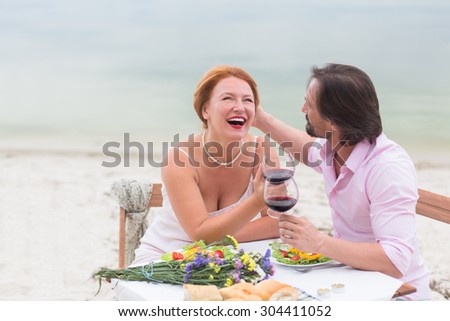 Beautiful couple sitting at the table in the restaurant isolated on sea. Woman with red hair communicating with her husband.