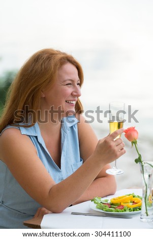 Close-up profile of beautiful mature woman smiling. Woman with red hair holding glass of white wine in the evening.