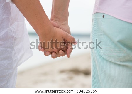 Couple walking on the beach and holding hands. Beautiful people spending their time near by sea during the sunset.