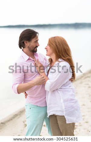 Attractive middle-aged couple in love spending time outdoors. People hugging, looking face to face and walking at the beach.