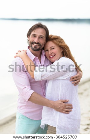 Caucasian couple hugging at the beach. Happy middle-aged man and woman smiling and enjoying each other\'s in the evening.