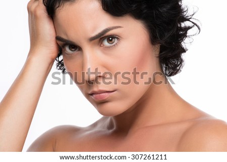 Close-up portrait of young lady posing with serious face on white background. Lady with black hair touching her head.