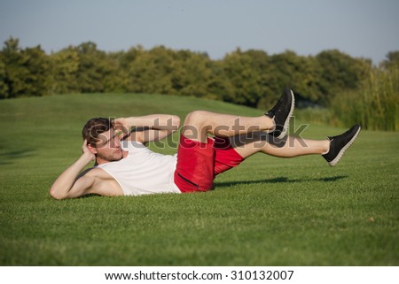 Healthy lifestyle concept. Fitness male athlete working out cross training ongreen grass. Man in red shorts doing crunch abdominals exercise.