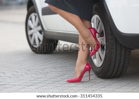 Businesswoman posing near white car and showing her slim and slender legs near her car. Successful lady in grey skirt posing on pink high heels.