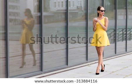 Fashion girl walking in the city and using her mobile phone. Pretty lady in little yellow dress wearing black high heels.
