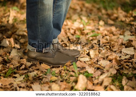 Man\'s legs on autumn leaves outdoors. Man in jeans and boots walking alone along the path in the park.