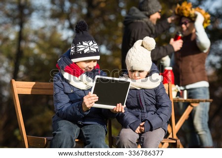 Little children sitting all together and looking through pictures or photos on the tablet PC. Whole family spending their time on a picnic.