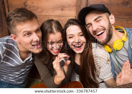 Two men and two ladies spending their free time in karaoke. Modern people singing songs and happy smiling for the camera.