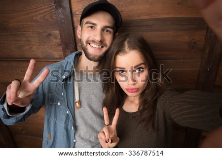 Bearded man and brunette lady showing yo signs and posing for the mobile phone\'s camera. People making selfies isolated on wooden background.